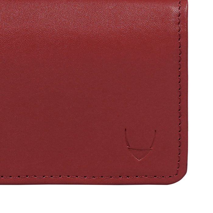 Close-up of red leather card holder showing smooth texture, stitched edges and subtle embossed logo.