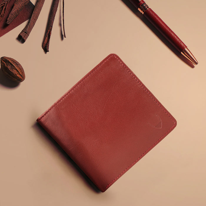 Men's red leather bifold wallet placed beside pen & accessories, stylish premium everyday accessory
