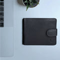 Black bi-fold leather wallet by Hidesign placed on a modern desk beside a laptop and a plant setup.