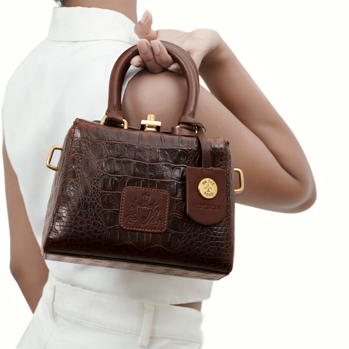 A Woman holding a Hidesign Ritz 01 brown croc-embossed sling bag with top handles and gold hardware.